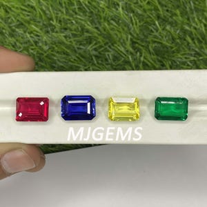 Puede incluir: Cuatro piedras preciosas rectangulares sobre una superficie blanca. Las piedras preciosas son roja, azul, amarilla y verde. El texto "MJGEMS" está impreso debajo de las piedras preciosas.