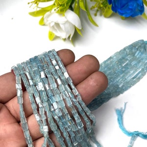 Puede incluir: Una hebra de cuentas de piedra preciosa de aguamarina azul claro, cada cuenta es rectangular y facetada. Las cuentas están enhebradas en un hilo transparente y tienen aproximadamente 6 mm de tamaño.