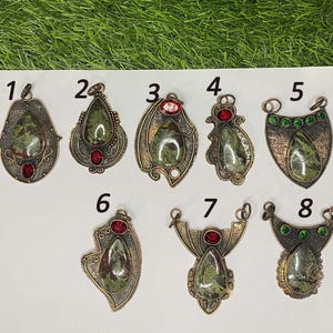May include: A collection of eight handcrafted pendants. Each pendant features a green and brown stone, accented with red or green gemstones. The pendants have intricate metalwork in various shapes, including teardrops and shields.