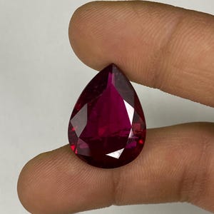 May include: A deep red pear-shaped gemstone with a faceted cut.