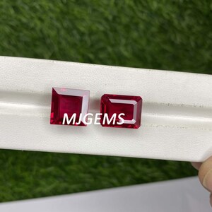 May include: Two red gemstone squares, one with a slightly rectangular shape, on a white surface. The text "MJGEMS" is visible in the center of the image.