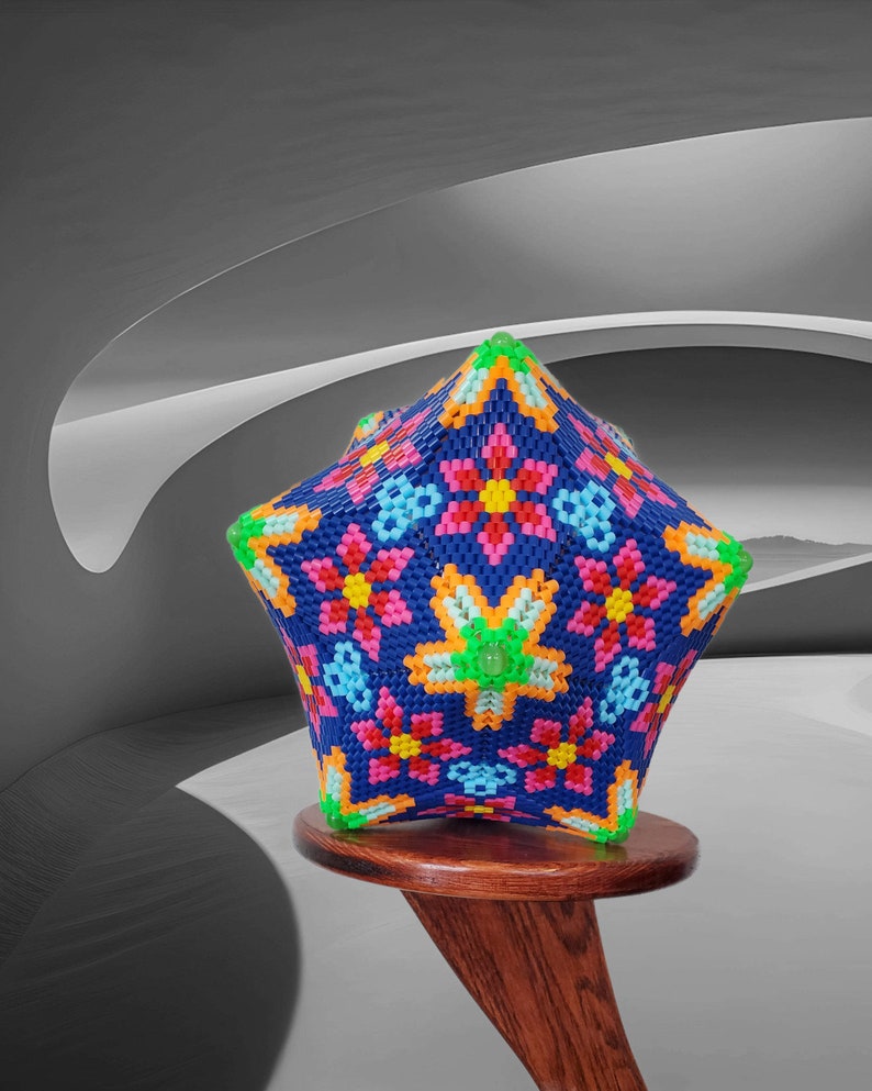 Puede incluir: Un adorno de cuentas con forma de estrella multicolor con un patr&oacute;n floral. El adorno est&aacute; hecho de peque&ntilde;as cuentas de colores y se muestra en un soporte de madera.