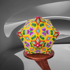 Puede incluir: Una escultura de cuentas geom&eacute;trica y colorida con una base en forma de estrella. La escultura est&aacute; hecha de peque&ntilde;as cuentas de colores en tonos de amarillo, verde, rojo, morado y naranja. Est&aacute; sentada en un taburete de madera.