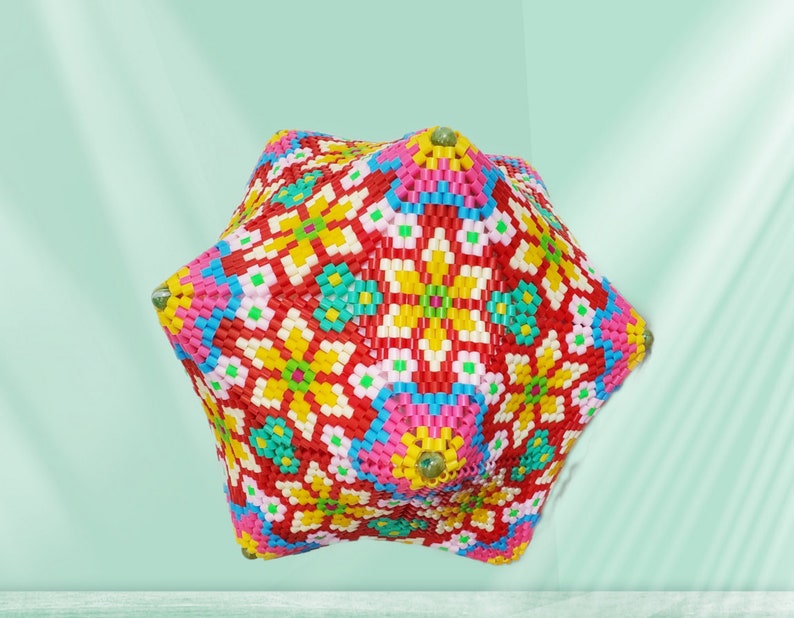 Puede incluir: Un objeto tridimensional geom&eacute;trico y colorido hecho de cuentas de pl&aacute;stico. El objeto tiene la forma de un cubo con bordes redondeados y est&aacute; decorado con un patr&oacute;n repetitivo de flores y formas geom&eacute;tricas. El objeto es una mezcla vibrante de rojo, amarillo, azul, verde, rosa y blanco.