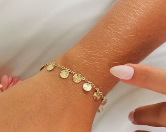 Puede incluir: Un brazalete dorado con una cadena delicada y pequeños abalorios redondos texturizados.