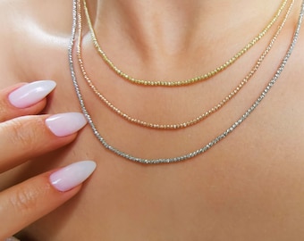 May include: Three layered necklaces with different colored metal beads. The top layer is gold, the middle layer is rose gold, and the bottom layer is silver.
