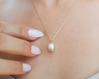May include: A delicate gold chain necklace with a single white pearl pendant encased in a gold wire cage.