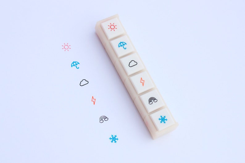 May include: A white plastic stamp set with six different weather icons: sun, umbrella, cloud, lightning bolt, rainbow, and snowflake. The icons are in different colors, including red, blue, orange, and black.
