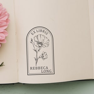 May include: A book with a black and white stamp on the inside cover. The stamp features a stylized flower with the text "Ex Libris Rebecca Long".
