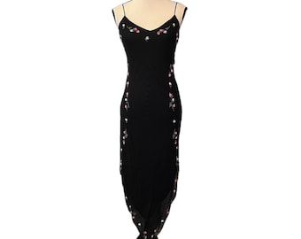 May include: A black, floor-length dress with spaghetti straps and a V-neck. The dress is adorned with delicate floral embroidery in pink and white. The dress is displayed on a mannequin.