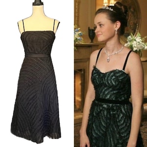 May include: A black strapless dress with a textured, wave-like pattern. The dress has a fitted bodice, a thin belt at the waist, and a knee-length skirt. The dress is displayed on a mannequin. A second image shows a person wearing a similar dress.