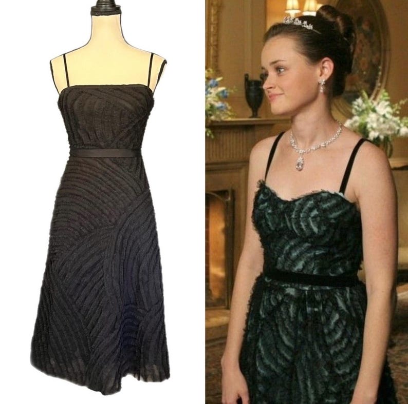 May include: A black strapless dress with a textured, wave-like pattern. The dress has a fitted bodice, a thin belt at the waist, and a knee-length skirt. The dress is displayed on a mannequin. A second image shows a person wearing a similar dress.
