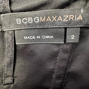 May include: Close-up of a black garment with a label that reads "BCBGMAXAZRIA" in white and gold lettering. Below the brand name, the label states "MADE IN CHINA." A separate tag indicates the size is "2."