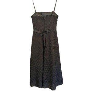 May include: A dark brown, textured midi dress with thin spaghetti straps. The dress features a square neckline, a fitted bodice, and a flowing skirt. A matching fabric belt cinches the waist. The back of the dress has a zipper closure.