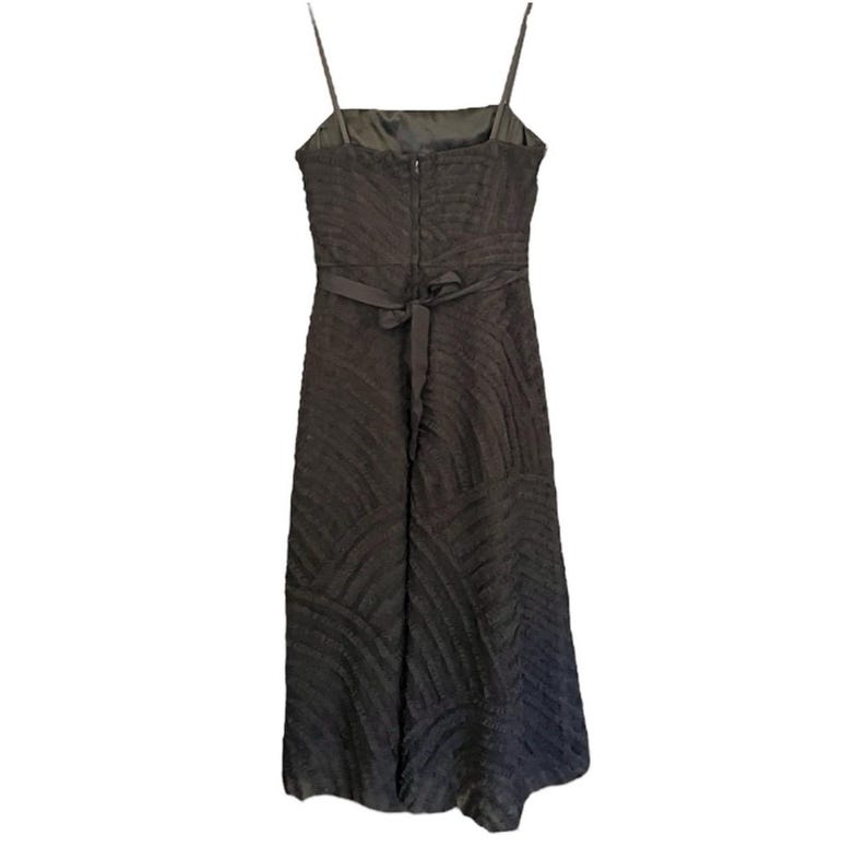 May include: A dark brown, textured midi dress with thin spaghetti straps. The dress features a square neckline, a fitted bodice, and a flowing skirt. A matching fabric belt cinches the waist. The back of the dress has a zipper closure.