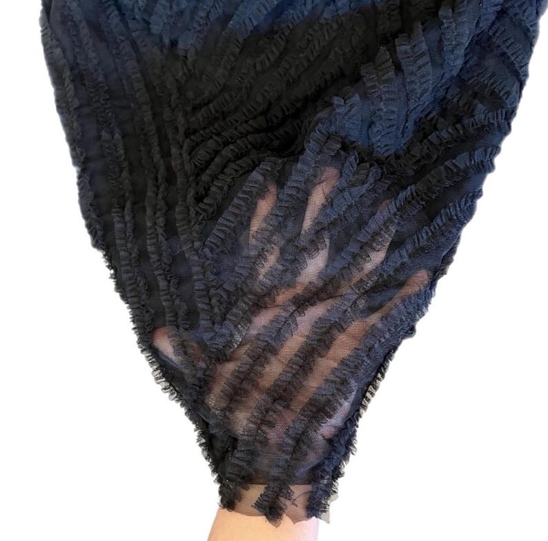 May include: A dark gray, sheer fabric with a ruffled texture. The fabric is arranged in a diagonal pattern, creating a layered effect. The material appears lightweight and delicate, suitable for apparel or decorative purposes.