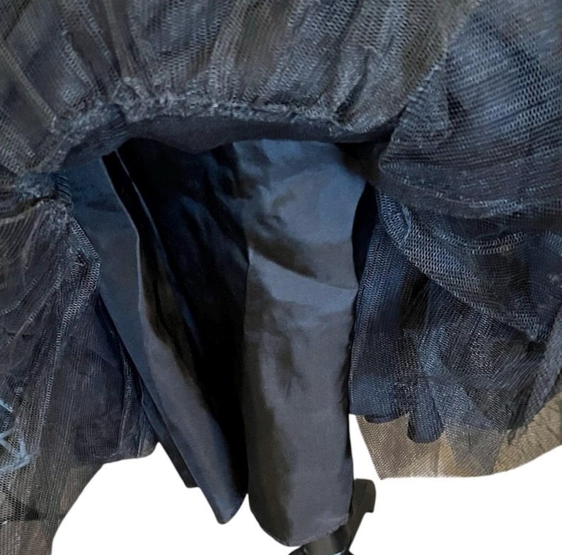 May include: A black tulle skirt with a satin lining. The skirt has multiple layers of sheer tulle, creating a voluminous effect. The satin lining provides a smooth, opaque base. The skirt is designed to be worn at the waist.