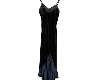 May include: A black velvet dress with spaghetti straps and a V-neckline adorned with small beads. The dress has a flowing, floor-length design with a layered, ruffled hem. The dress is hanging on a white hanger.