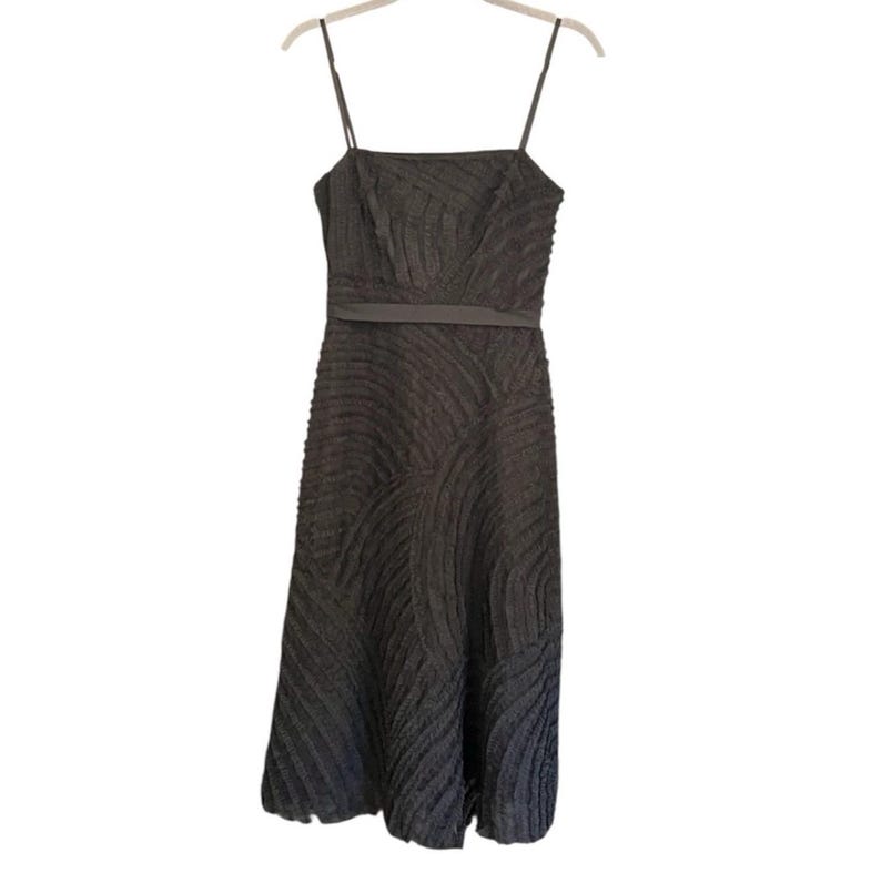 May include: A dark gray midi dress with thin spaghetti straps. The dress features a textured, patterned design and a thin belt at the waist. The dress is hanging on a hanger against a white background.