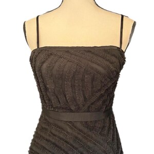 May include: A dark brown, strapless dress with a textured, ruffled design. The dress features thin spaghetti straps and a matching belt around the waist. The fabric has a layered, diagonal pattern.