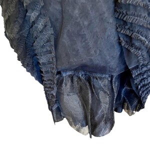 May include: A dark navy blue garment with layered, textured fabric. The design features ruffled edges and a sheer, flowing material, creating a layered effect. The garment appears to be a skirt or dress.