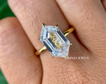 May include: A gold ring with a large, clear, octagon-shaped gemstone. The ring is on a finger and the text "Trionza Jewels" is visible in the bottom right corner.