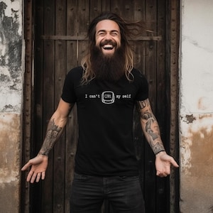Op de afbeelding: Een man draagt een zwart T-shirt met de tekst "I can't CTRL my self" in wit gedrukt. Hij lacht en heeft een lange baard.
