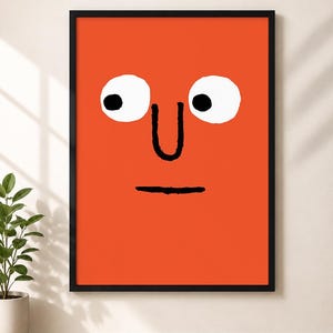 May include: A framed wall art print featuring a bright orange background with a simple black and white graphic face. The face consists of two large white circular eyes with black pupils, a black line for a nose, and a straight black line for a mouth.