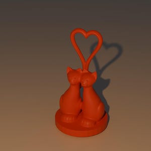 May include: Orange cat figurine with two cats facing each other, connected by a heart-shaped arch. The cats are sitting on a round base. The shadow of the heart is visible on the background.
