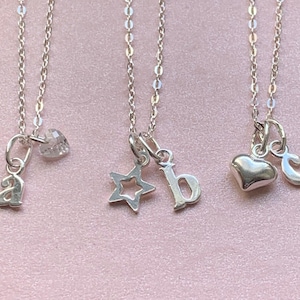 May include: Three silver necklaces with different charms. The first necklace has a letter 'a' charm. The second necklace has a star charm and a letter 'b' charm. The third necklace has a heart charm and a letter 'c' charm.