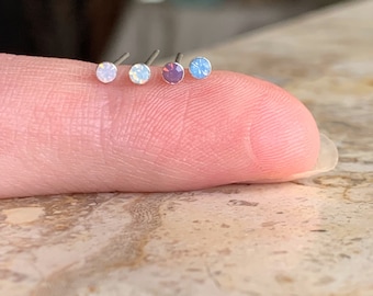 Puede incluir: Cinco tachuelas de nariz plateadas con pequeñas piedras preciosas redondas y de colores. Las piedras preciosas son en tonos de rosa, azul y morado.