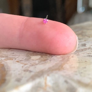 May include: A small pink gemstone nose ring with a silver post.