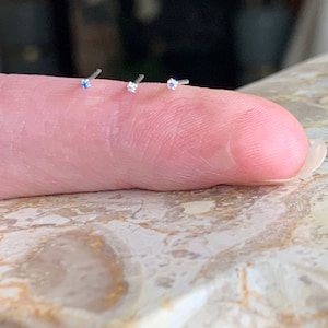 Peut inclure: Quatre anneaux de nez en argent avec de petits strass transparents.