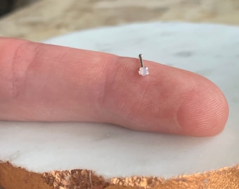 Puede incluir: Un aro de nariz de plata con una pequeña piedra cuadrada transparente.