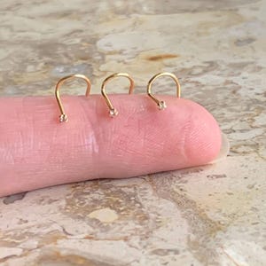 Op de afbeelding: Drie gouden neusringen met een kleine, heldere edelsteen op elke ring.