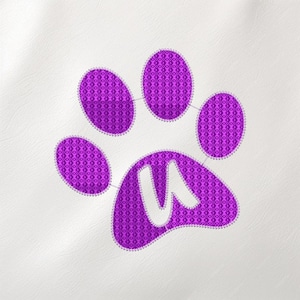 Puede incluir: Un diseño de huella de pata morada con la letra blanca "W" en el centro. La huella de la pata está bordada con un patrón texturizado y delineada con una puntada blanca. El fondo es una superficie blanca lisa.