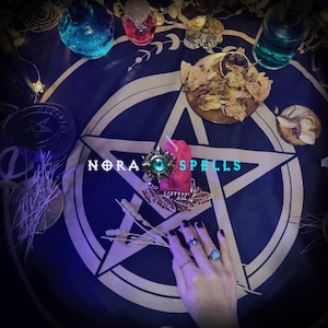May include: A mystical scene featuring a dark blue cloth with a white pentagram design. Various potion bottles, dried herbs, and a red candle are arranged around the cloth. The text "NORA SPELLS" is visible. A hand with rings is also present.