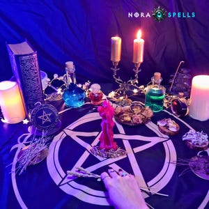 May include: A dark blue altar cloth featuring a white pentagram, topped with a red candle, a gold candelabra with two lit candles, glass bottles containing blue and green liquids, a vintage book, and dried herbs under the text NORA SPELLS.