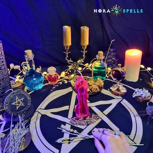 May include: A dark cloth featuring a white pentagram, a pink candle shaped like two figures embracing, a gold candelabra, glass bottles with blue and green liquids, a small red bottle, a pillar candle, and dried herbs under the text NORA SPELLS.