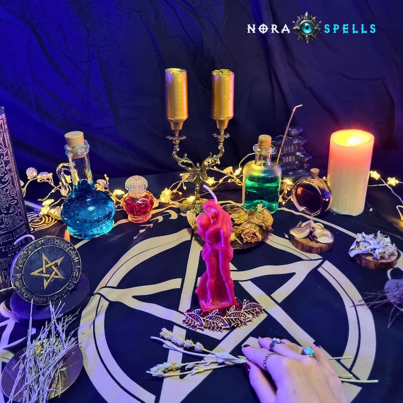 May include: A dark cloth featuring a white pentagram, a pink candle shaped like two figures embracing, a gold candelabra, glass bottles with blue and green liquids, a small red bottle, a pillar candle, and dried herbs under the text NORA SPELLS.