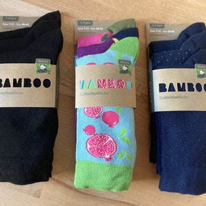 Pode incluir: Três pares de meias em padrões diferentes. As meias são pretas, azuis com bolinhas brancas e azuis com uma bainha verde e um padrão de romã rosa. As meias são embaladas em cartão com o texto "BAMBOO CollectionNiche" em cada embalagem.