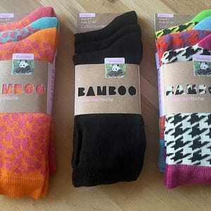 Può includere: Tre paia di calze da donna con motivi diversi. Le calze sono realizzate in bambù e sono confezionate in scatole marroni con il testo "Bamboo Collection Niche". Le calze sono di colore arancione, nero e bianco.