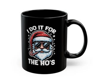 May include: Black ceramic mug featuring a Santa Claus graphic wearing sunglasses and a red hat. The text "I DO IT FOR THE HO'S" is printed on the mug. The mug has a curved handle.