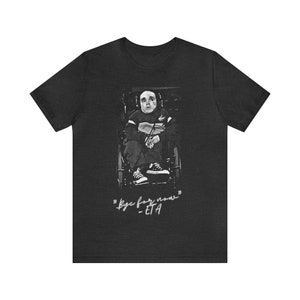 May include: Charcoal grey t-shirt with a black and white image of a person in a wheelchair with a painted face. The text "Bye for now" and "-ETA" are below the image.