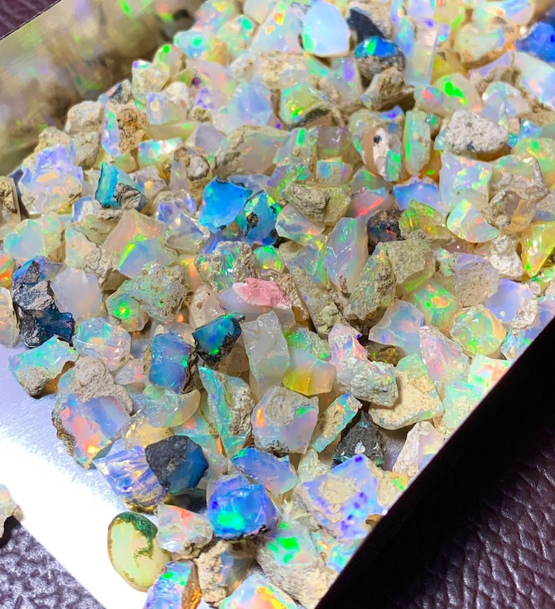 May include: A collection of rough opal gemstones in various sizes and shapes. The opals are a mix of white, grey, and iridescent colours.