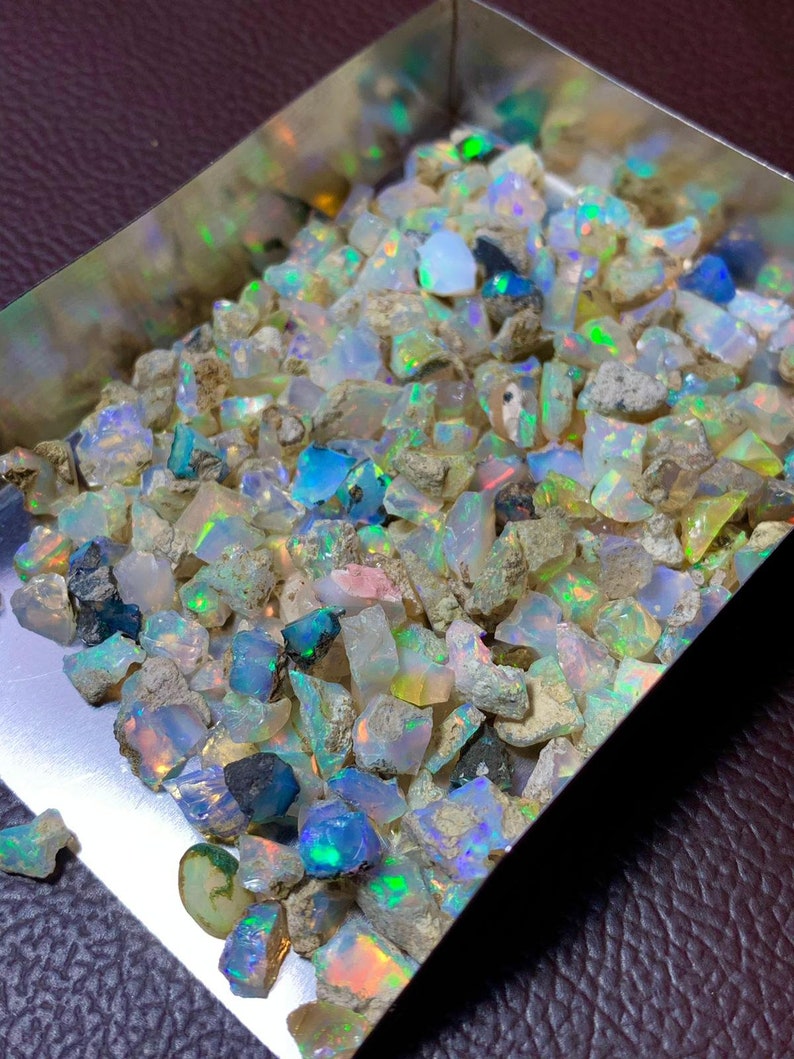 May include: A metal tray filled with a variety of small, iridescent opal gemstones. The opals are various shades of white, blue, green, and pink.