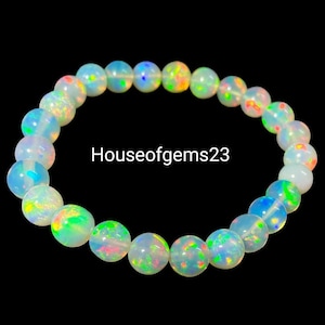 May include: A circular bracelet composed of smooth, round, translucent white beads with vibrant iridescent flashes of green, orange, and blue. The text Houseofgems23 is centered within the circular arrangement of the gemstone beads.