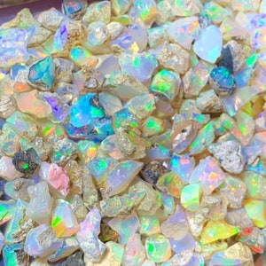 May include: A close-up view of a collection of iridescent opal gemstones. The opals are various shapes and sizes, with a mix of white, blue, green, and yellow hues.