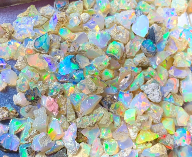 May include: A close-up view of a collection of iridescent opal gemstones. The opals are various shapes and sizes, with a mix of white, blue, green, and yellow hues.