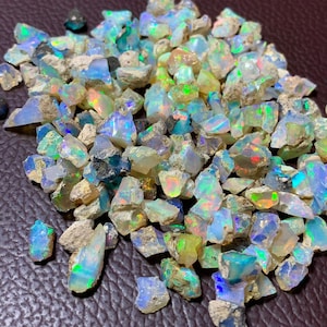 Peut inclure: Un tas de pierres précieuses d'opale brute, de différentes tailles et formes, aux reflets irisés. Les opales sont un mélange de blanc, de bleu, de vert et de jaune.